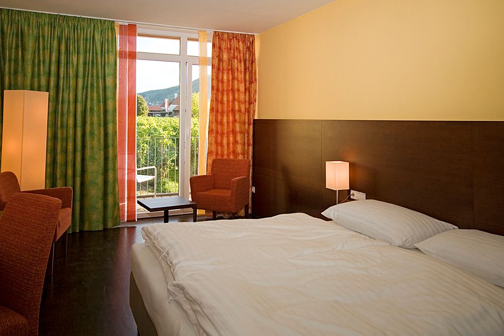 Hotel room with double bed, two armchairs, curtains and balcony with a view of the green landscape.