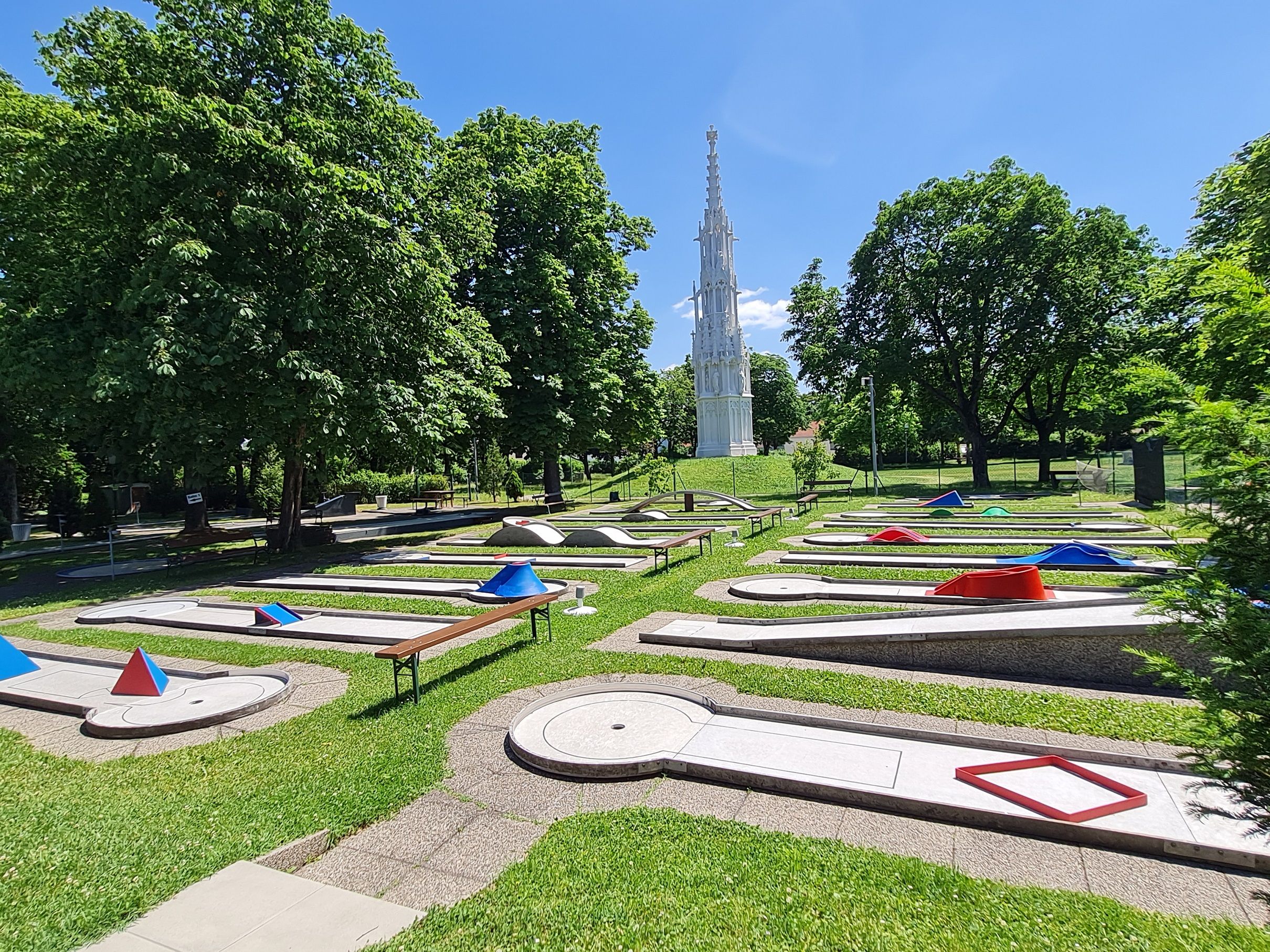 Minigolf course with obstacles and a high white tower in the background.