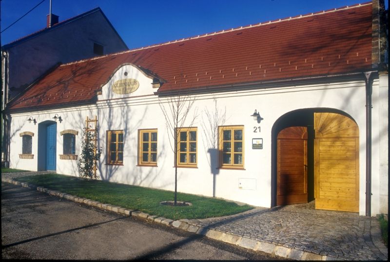 White building with red roof and wooden doors, labeled 'Kleinhaus'.