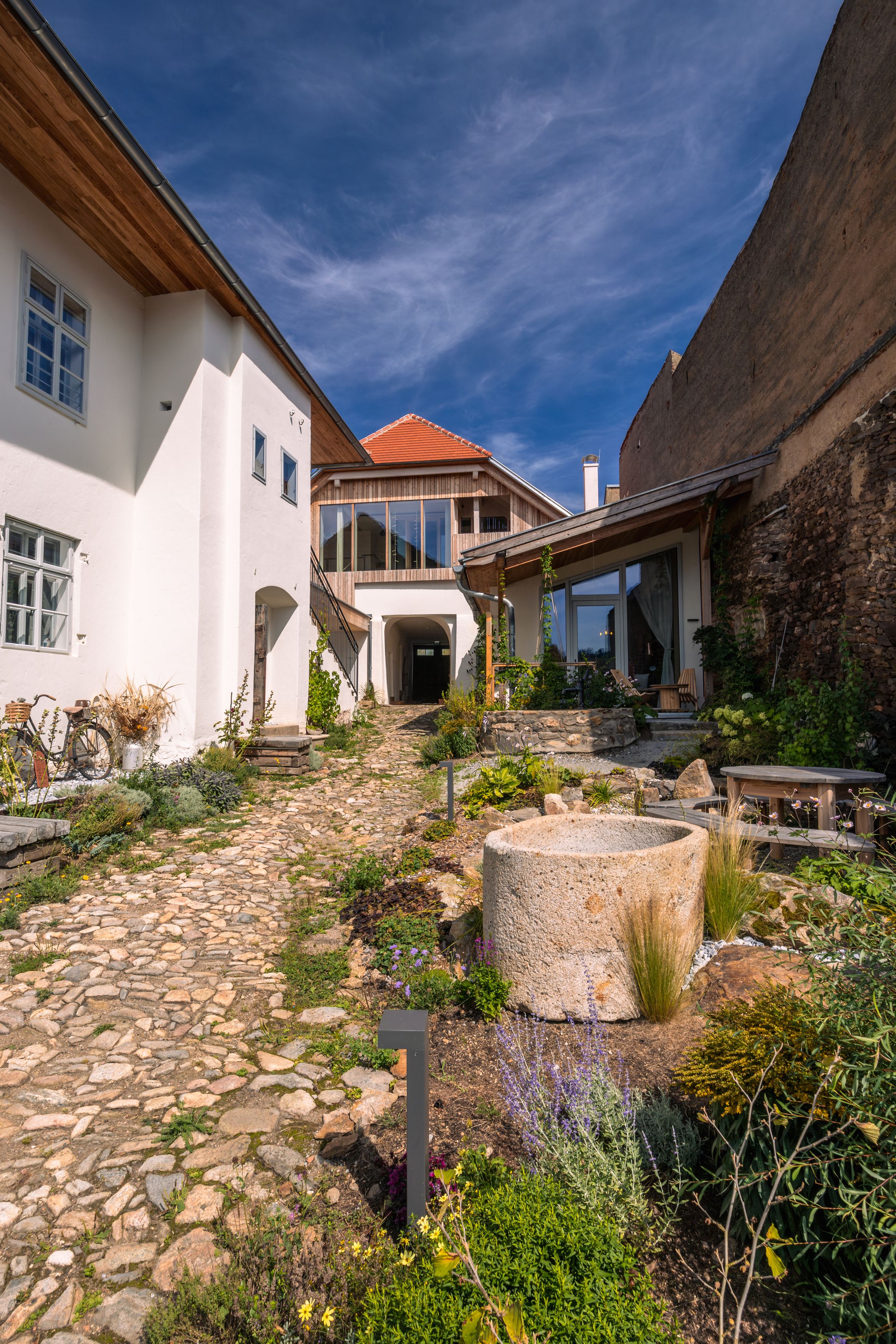 Inner courtyard with paved path, plants and modern buildings under a blue sky.