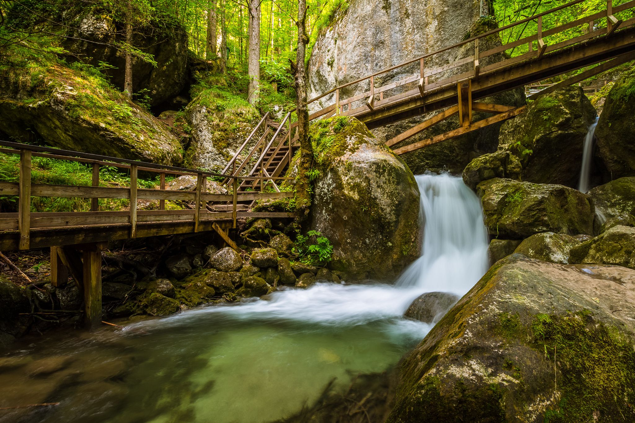 Waterfall with wooden bridges and steps in a wooded area.
