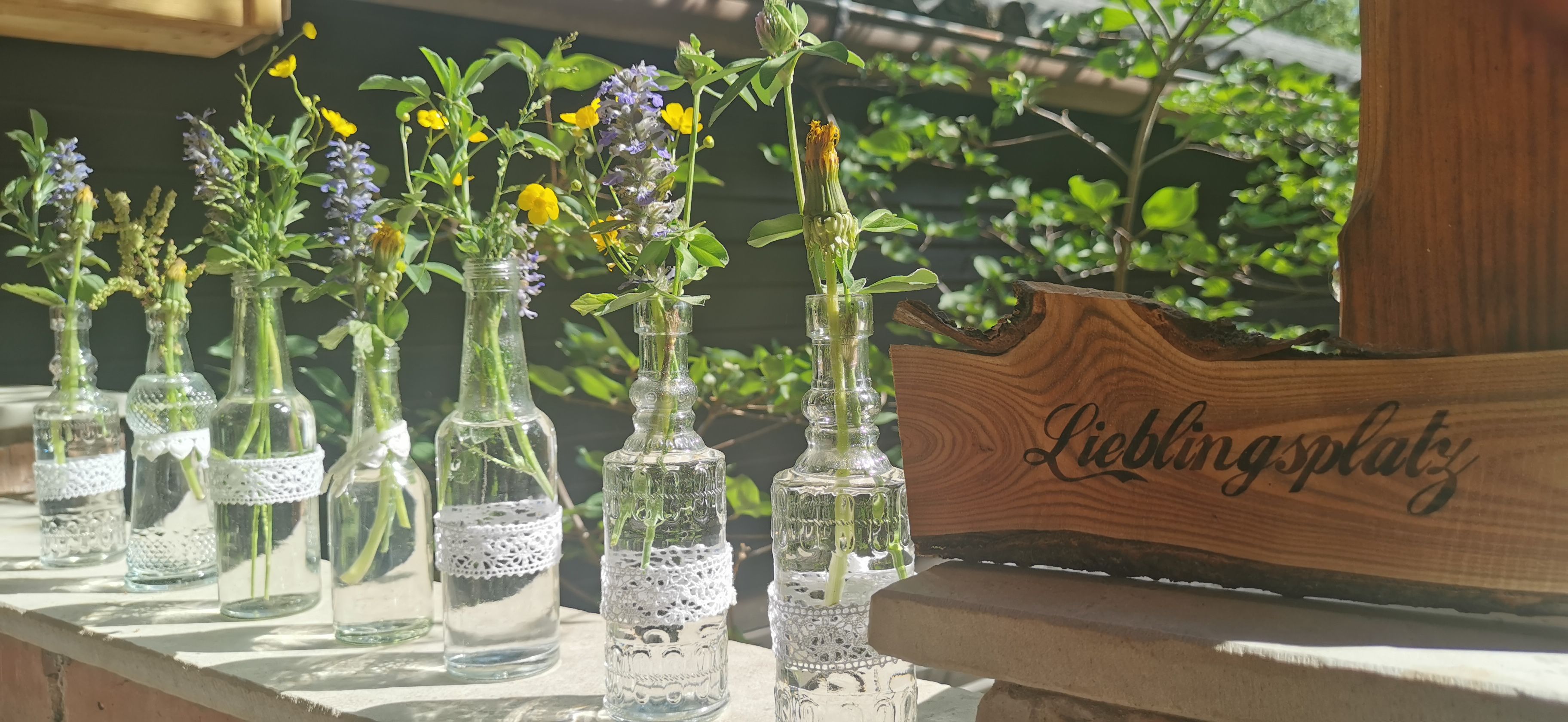 Small glass bottles with meadow flowers and a wooden sign with the inscription 'Favorite place'.