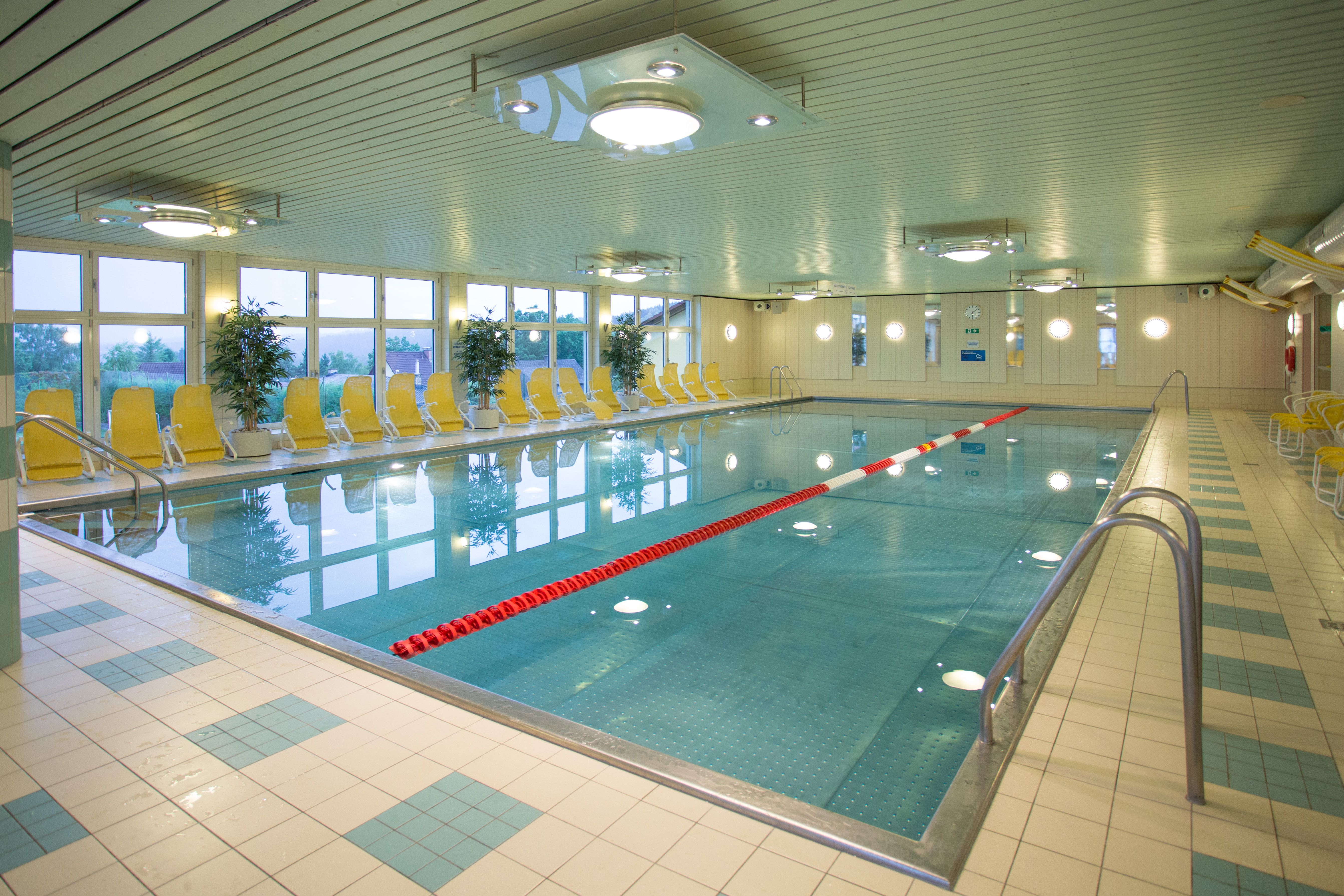 Interior view of an empty indoor pool with yellow deckchairs and plants.