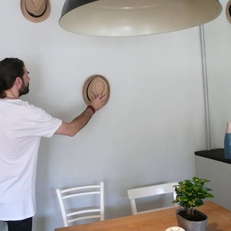 Person hangs straw hat on a wall with several hats.