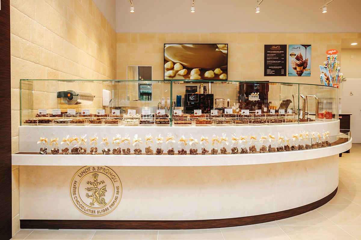 Interior view of a chocolate store with chocolates in glass display cases and a Lindt & Sprüngli logo.