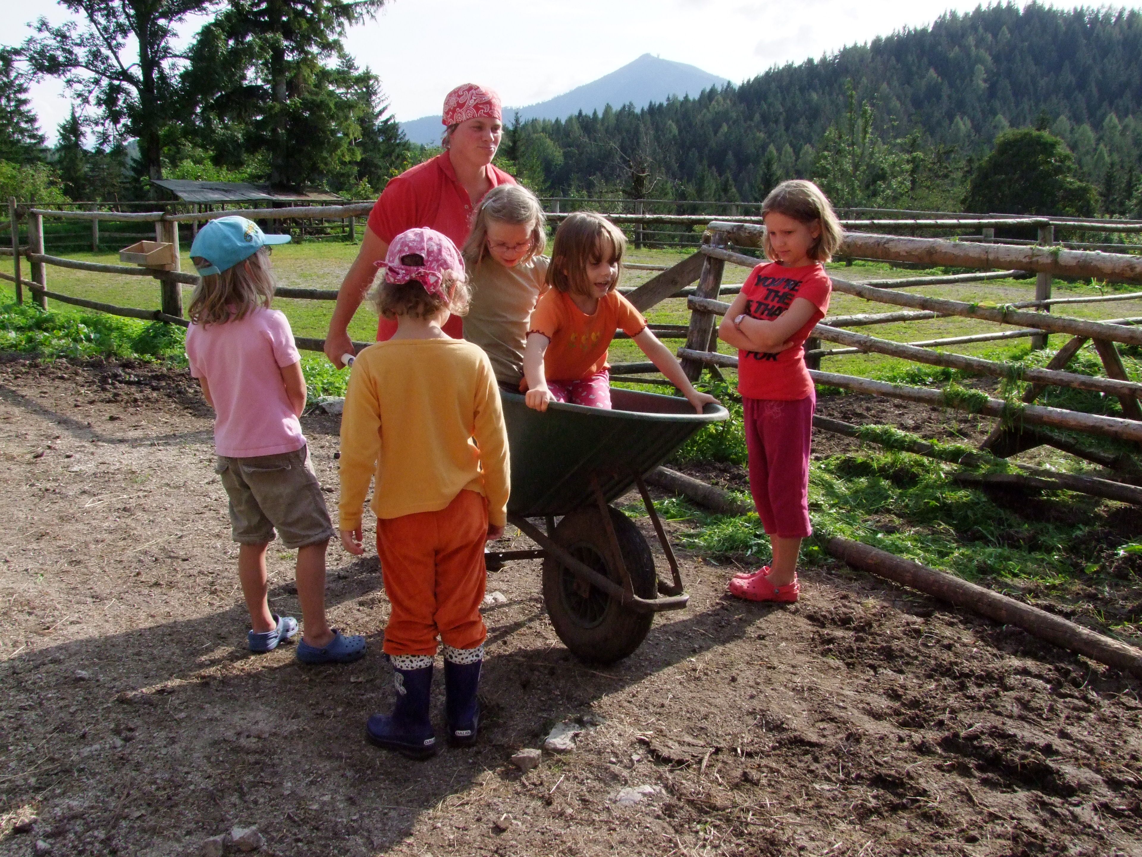 Children playing with a wheelbarrow on a farm.