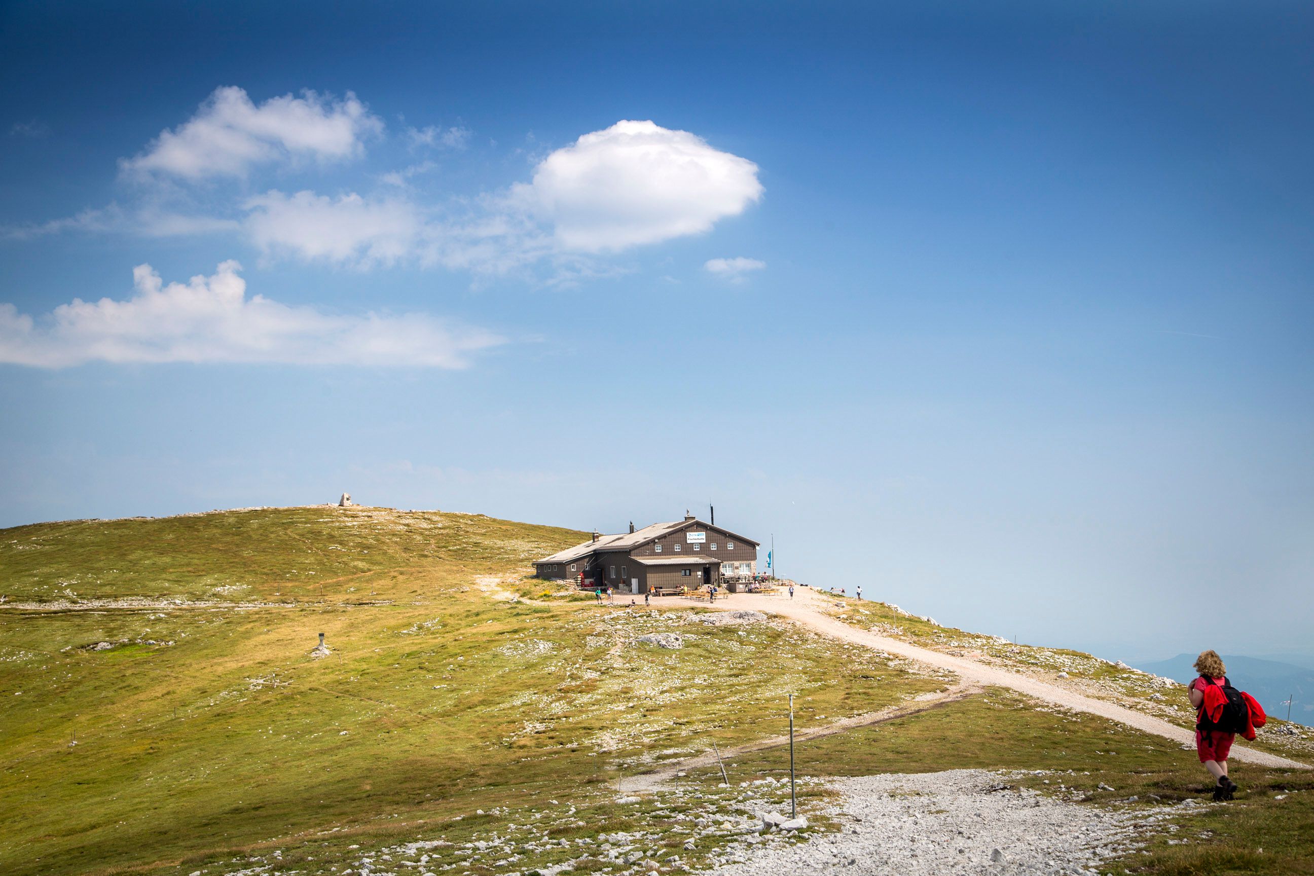 A mountain hut on a hill with a blue sky and clouds in the background.