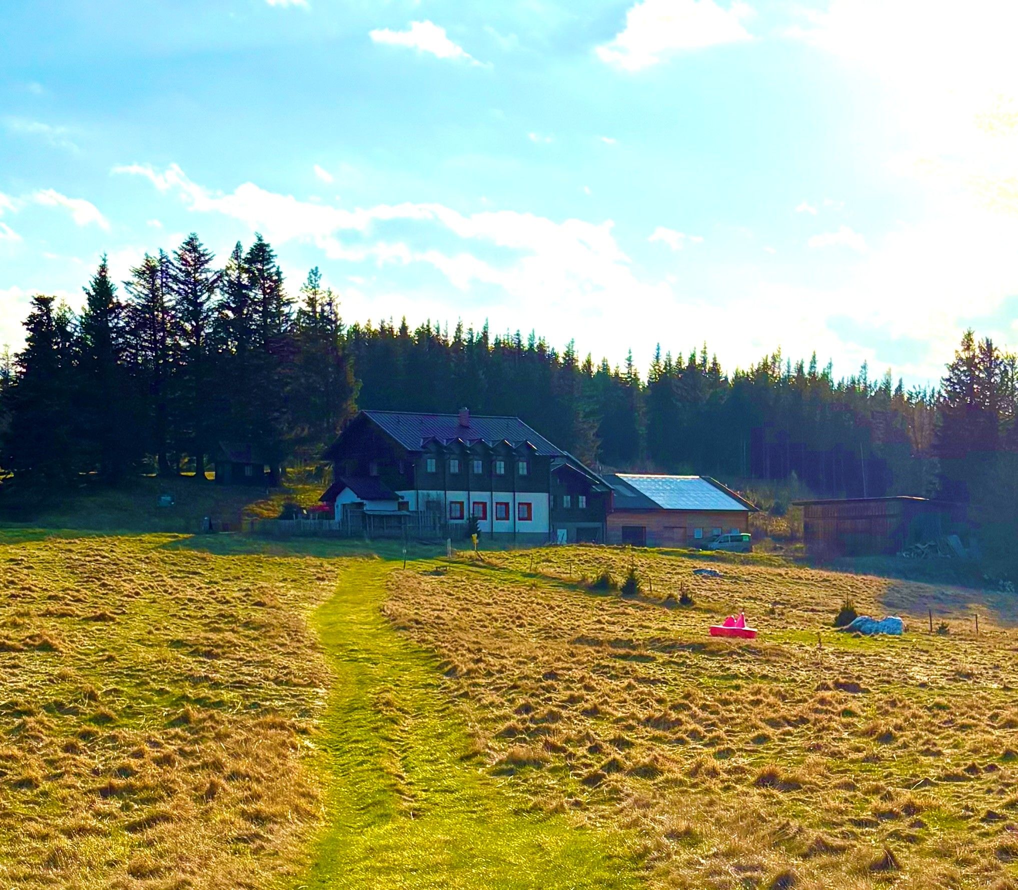 A farmhouse in a meadow, surrounded by trees and under a blue sky.