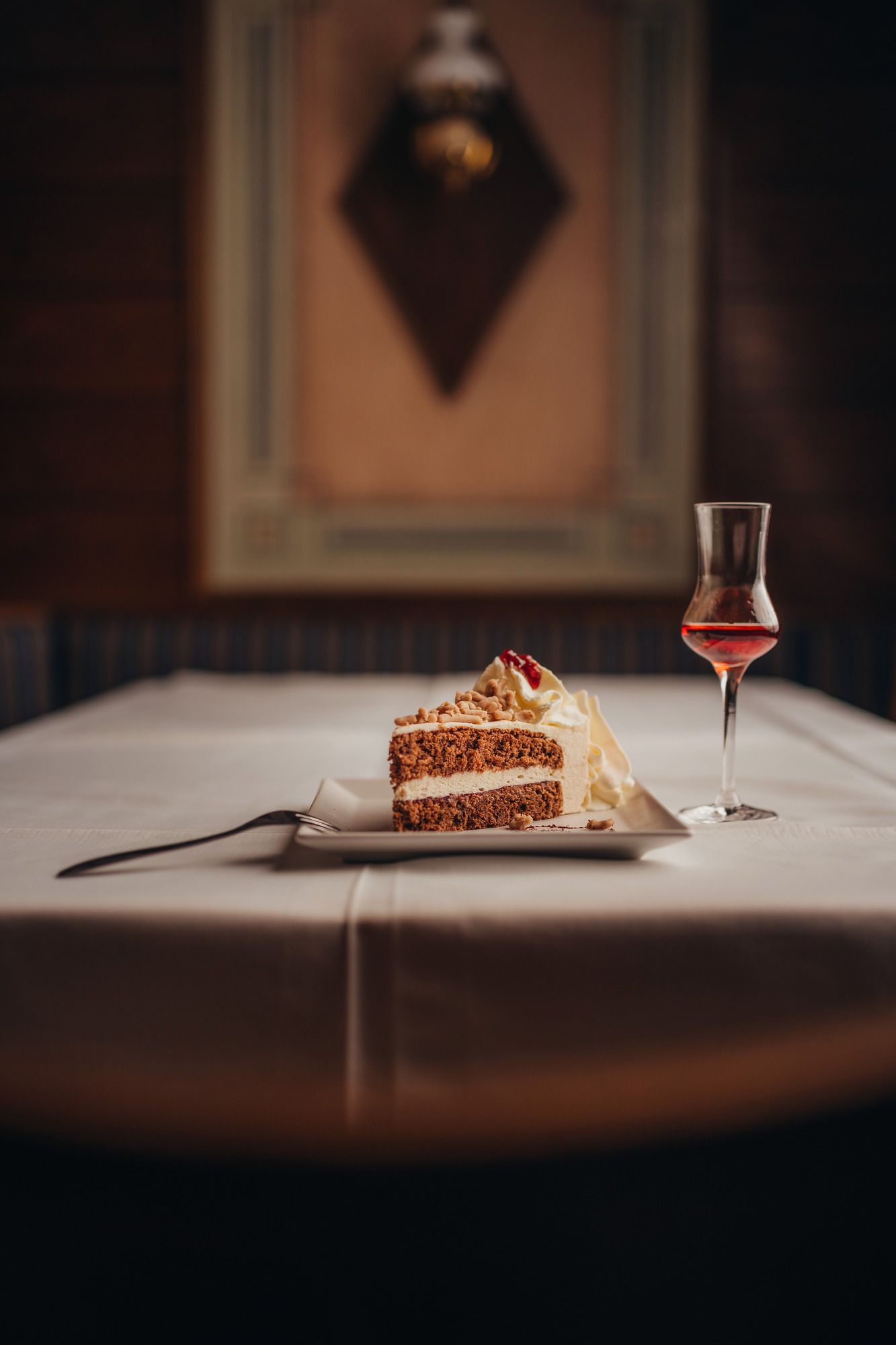 A slice of cake with cream and a glass of liqueur on a laid table.