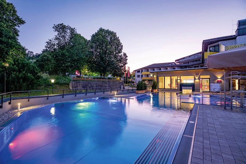 Illuminated pool area at night with buildings in the background.