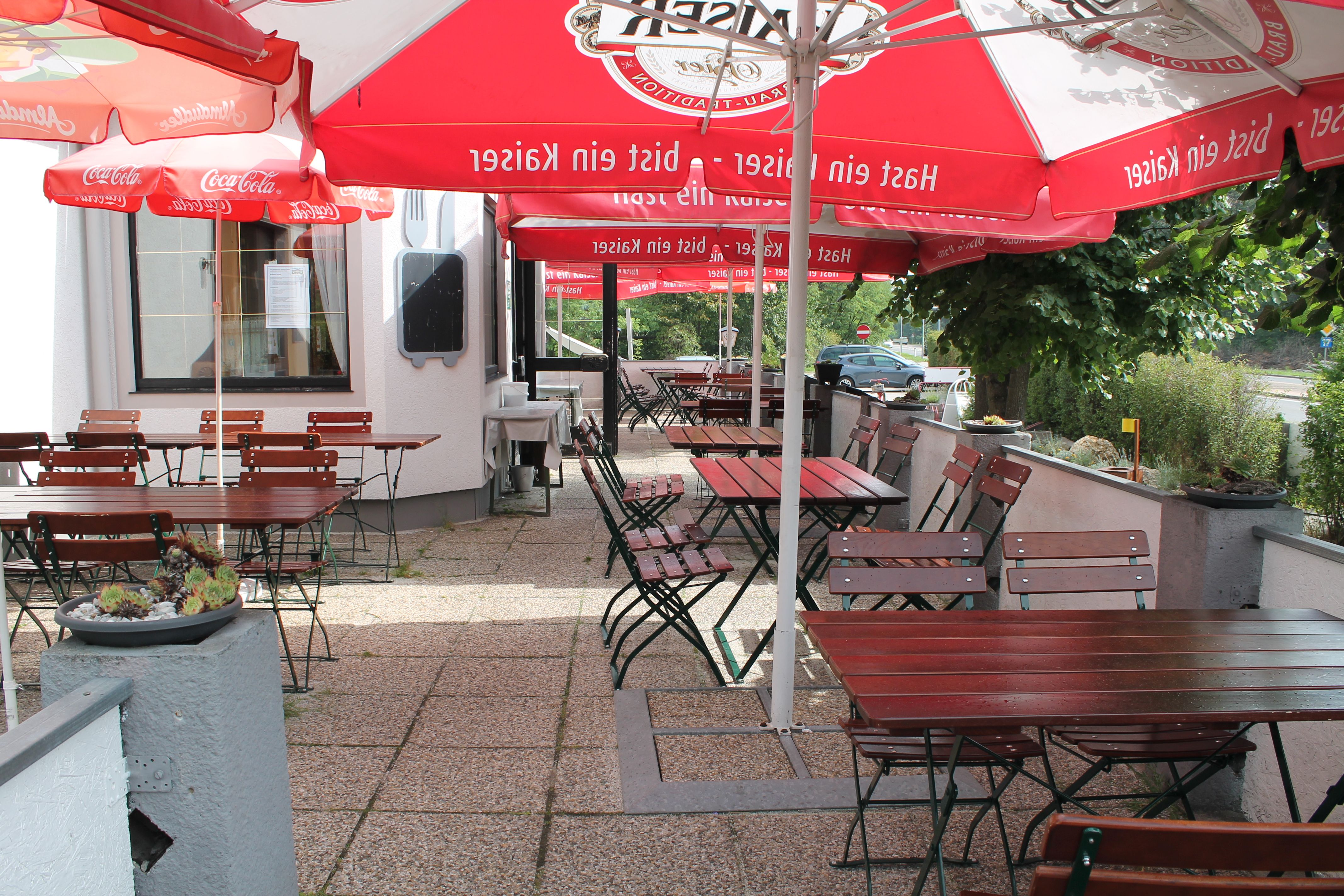 An empty guest garden with wooden tables and chairs under red parasols.