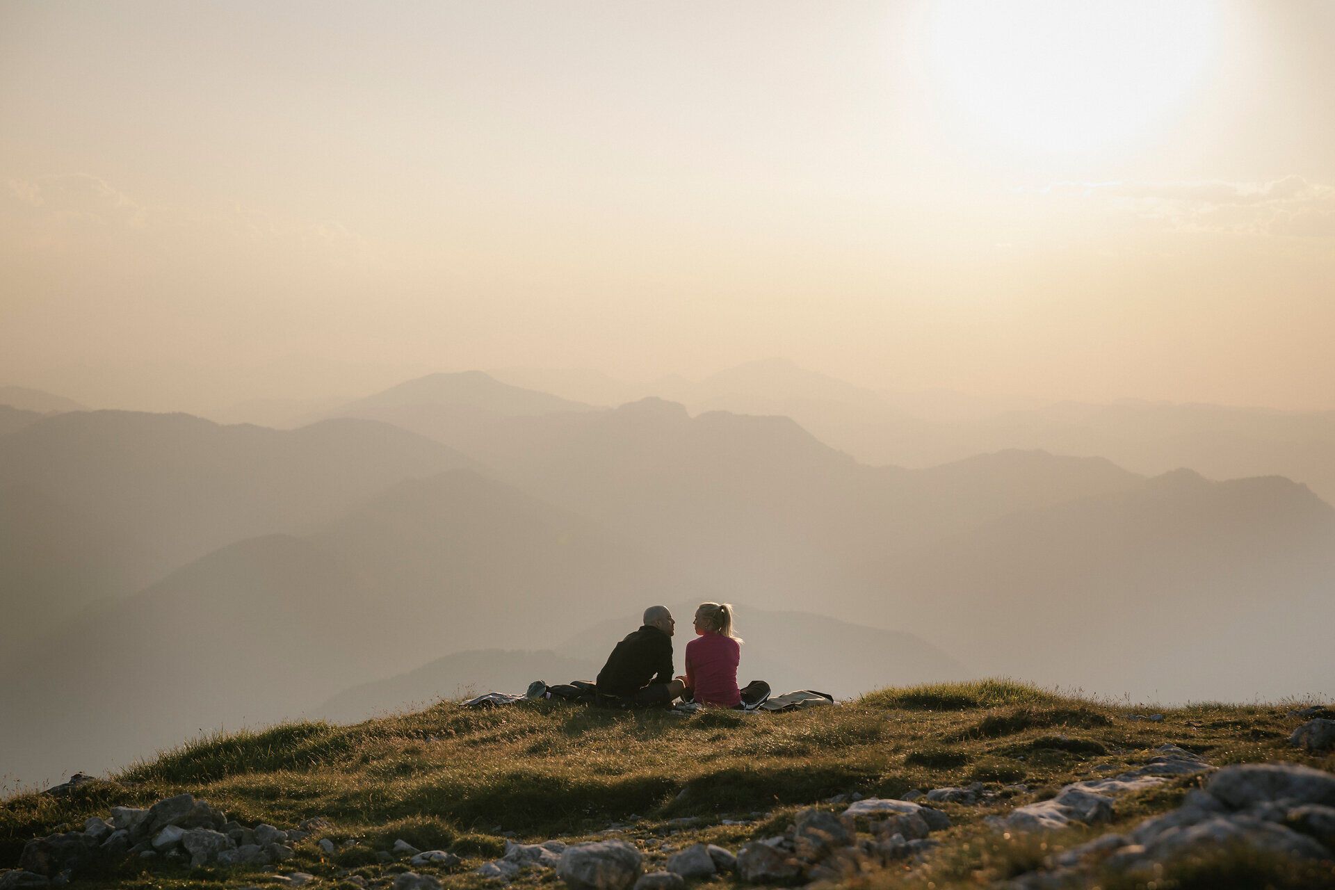 Two people are sitting in the evening light on a meadow near the Schneeberg, gazing out over the mountain landscape