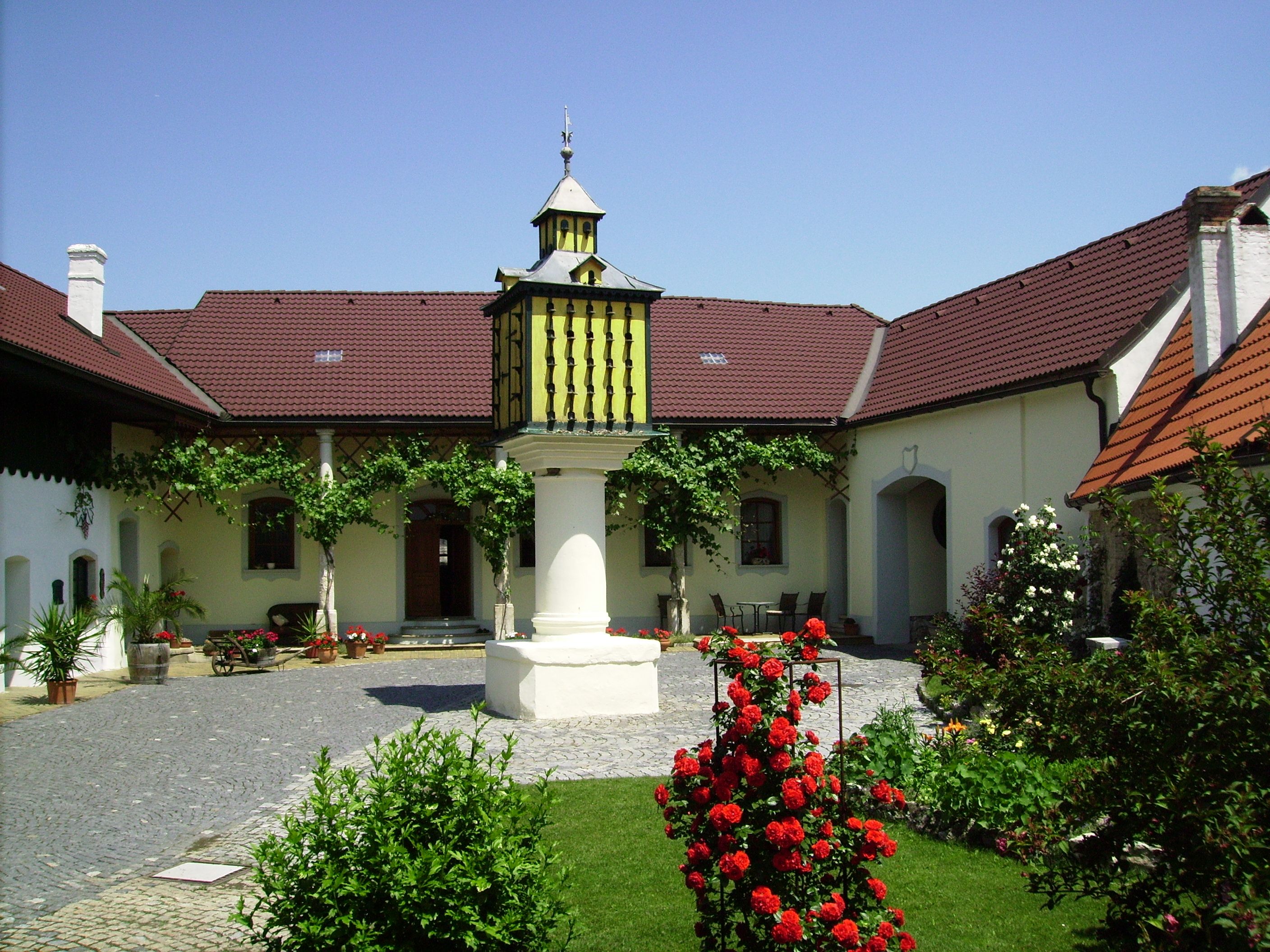 A well-kept courtyard with flowers, a central fountain and a building with red roofs.