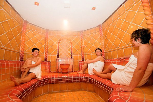 Three people in a tiled steam bath, wrapped in towels.