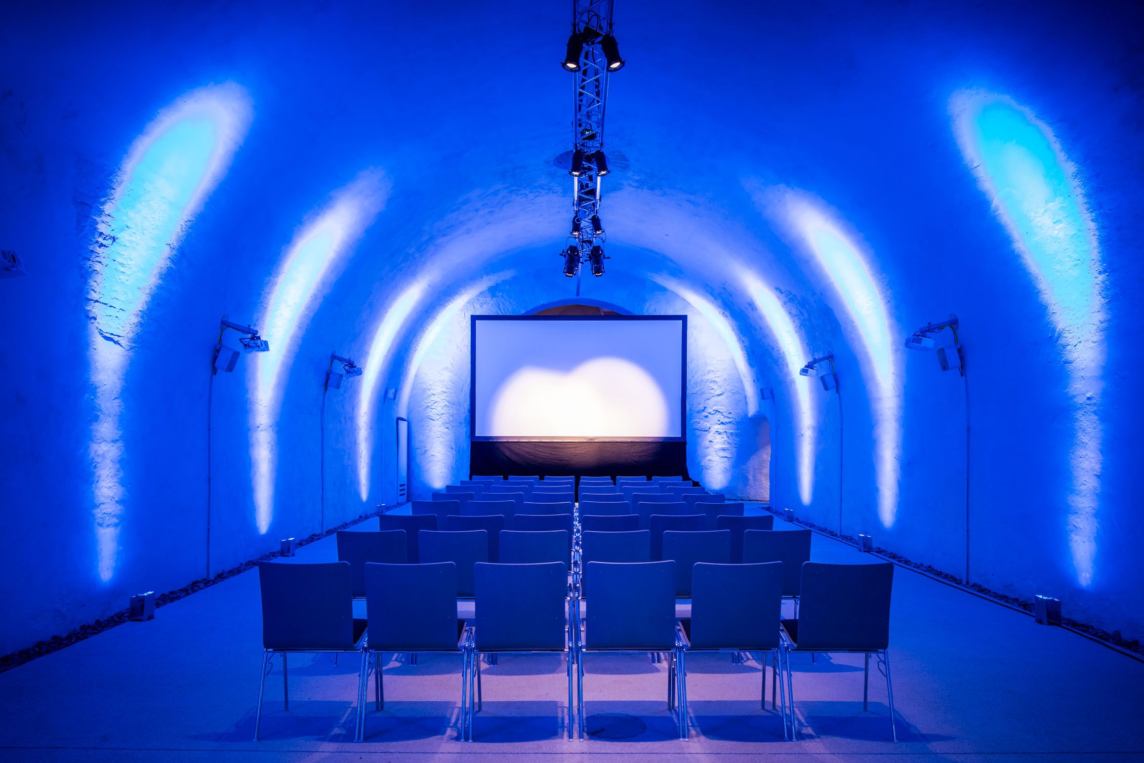 A bluish-lit room with cinema seating and a screen.