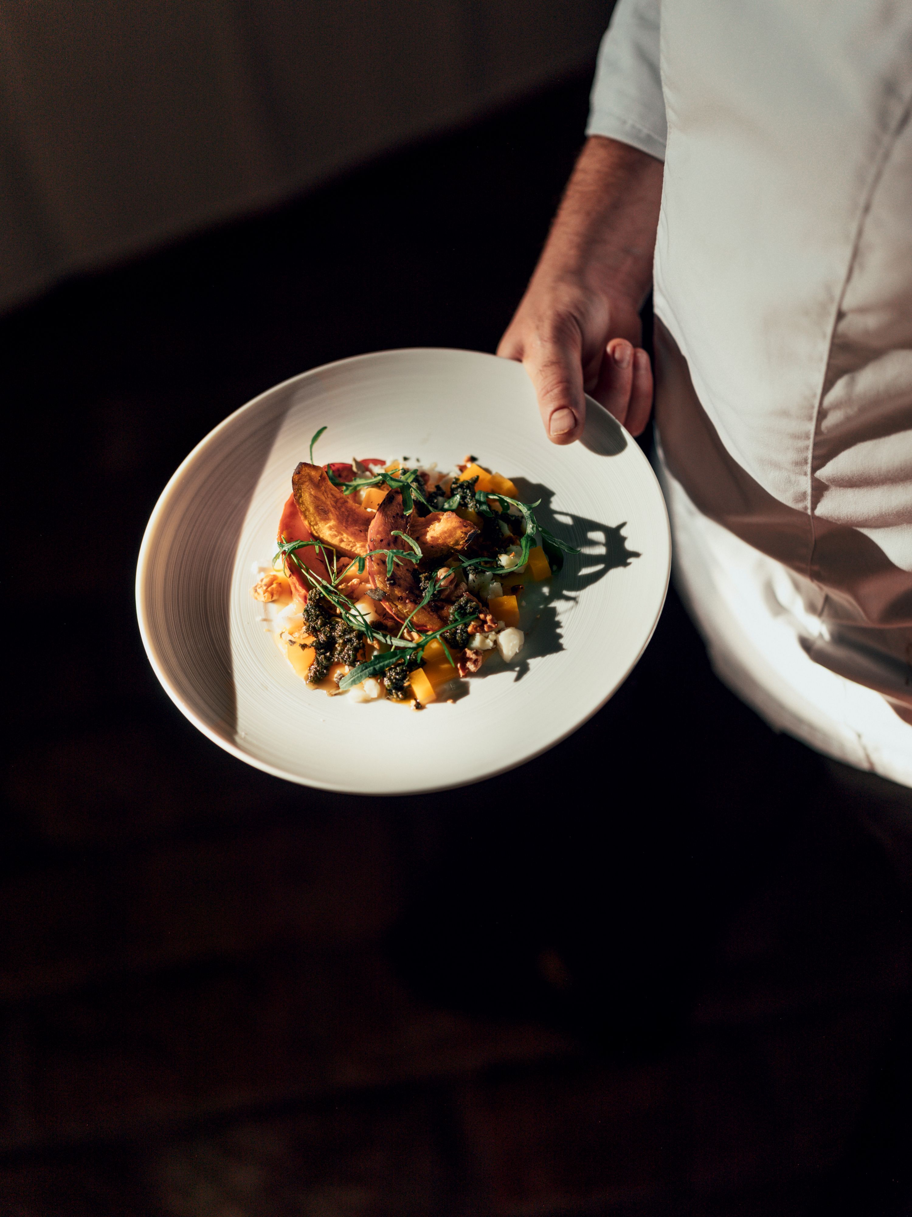A plate with an elaborately arranged dish is held by a person in white clothing.