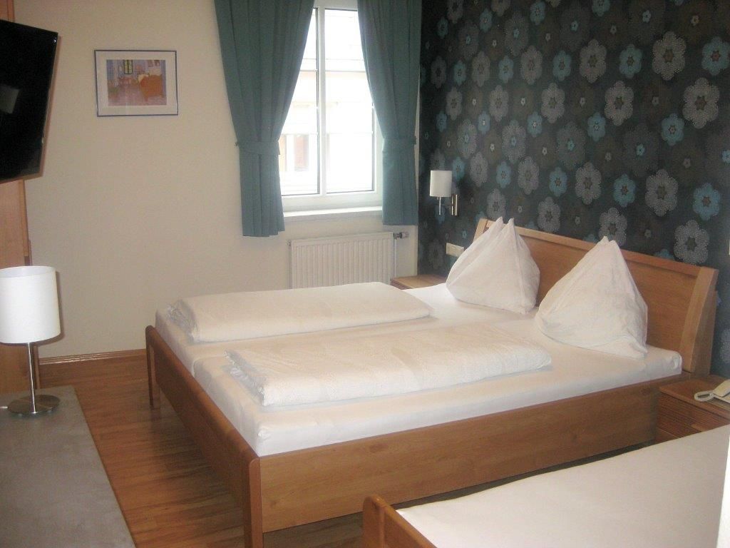 Hotel room with double bed, flowery wallpaper and windows with green curtains.