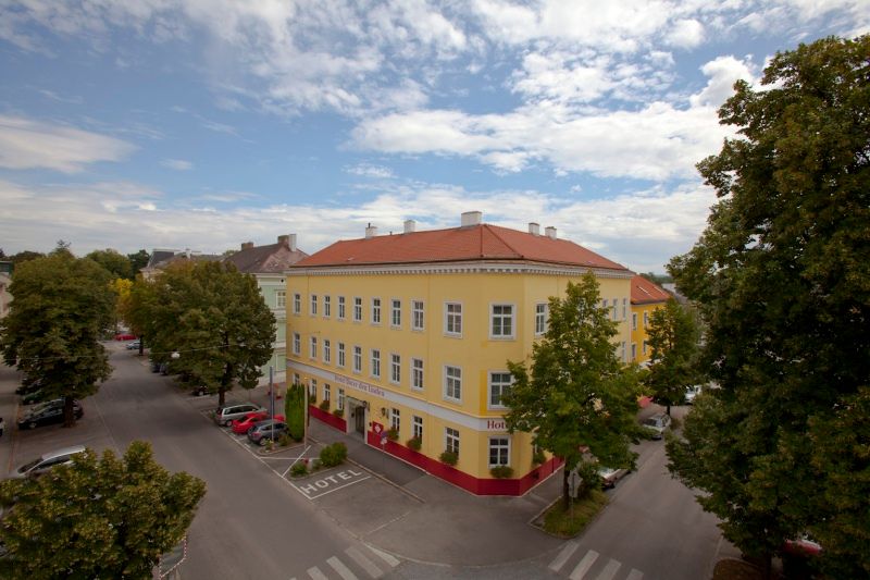 Exterior view of a yellow hotel with a red roof, surrounded by trees and streets.