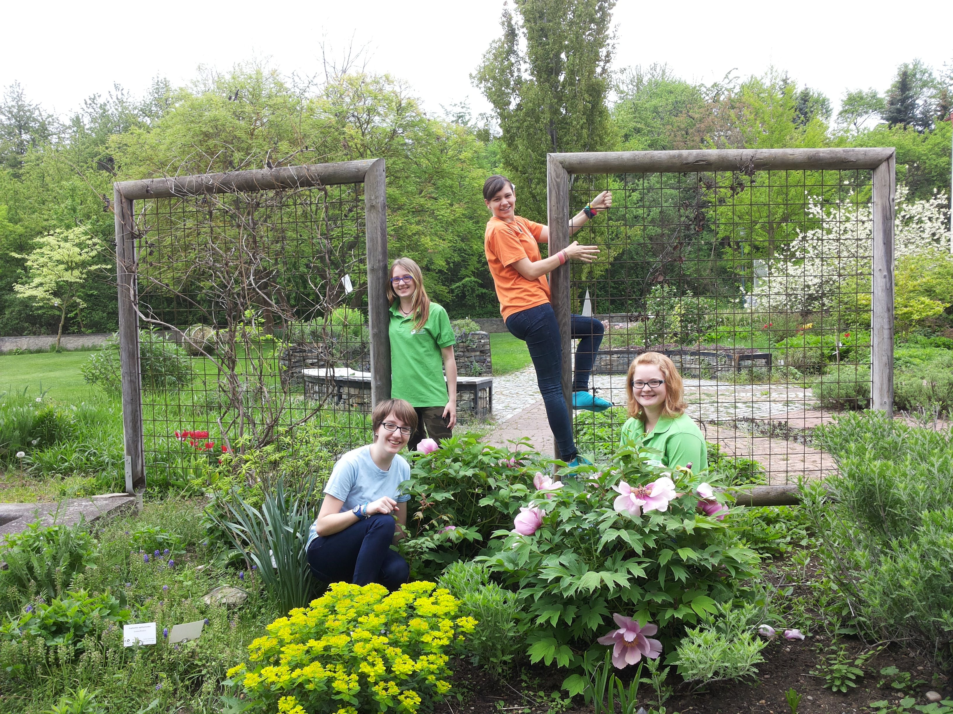 Four people in a garden with flowers and trellises.
