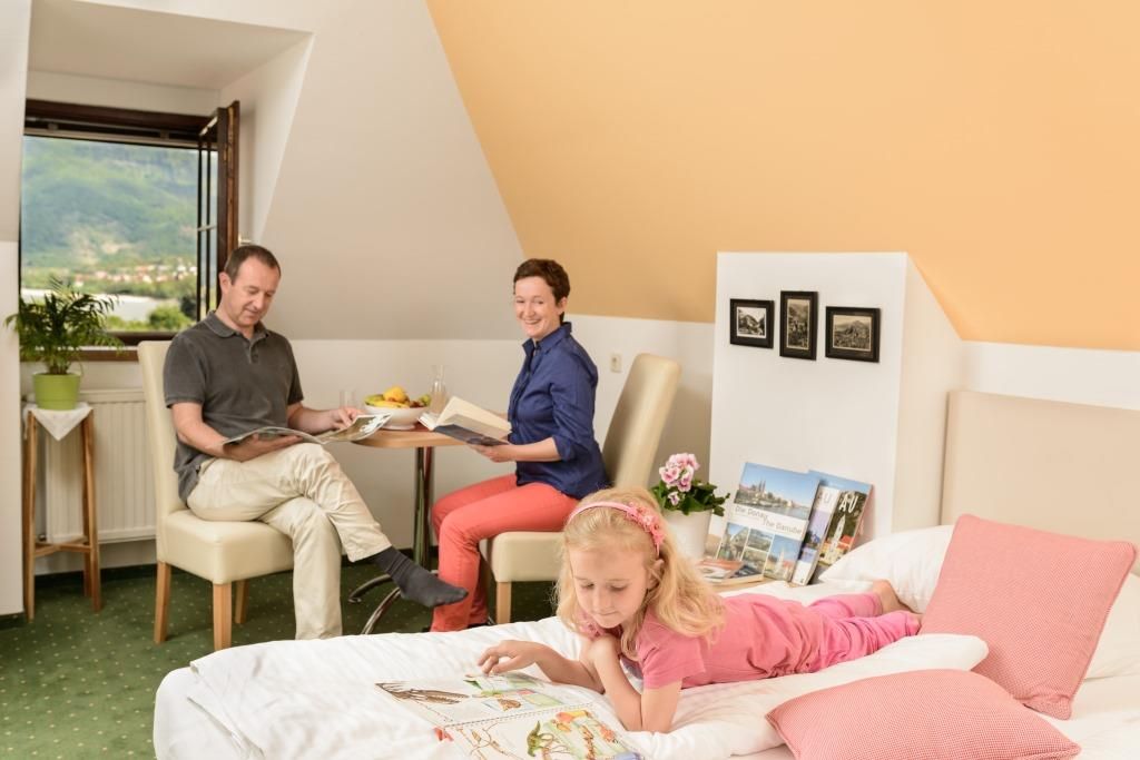 Family in a cozy room, parents reading at the table, child lying on the bed with a book.