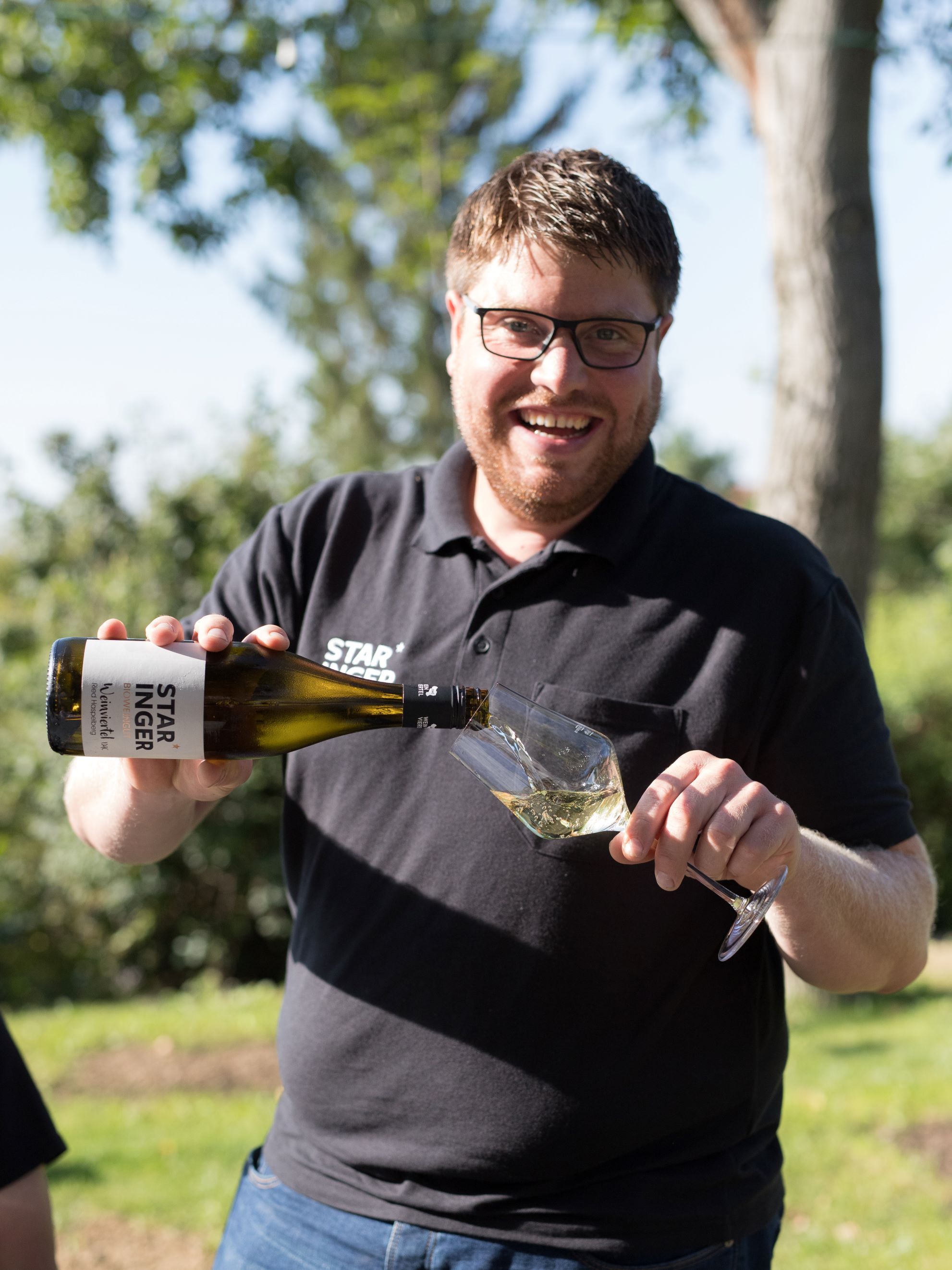 Man pouring wine into a glass outdoors.
