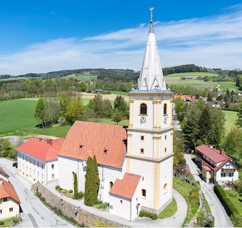 Aerial view of the fortified church of Krumbach in a rural setting with green fields and blue sky.