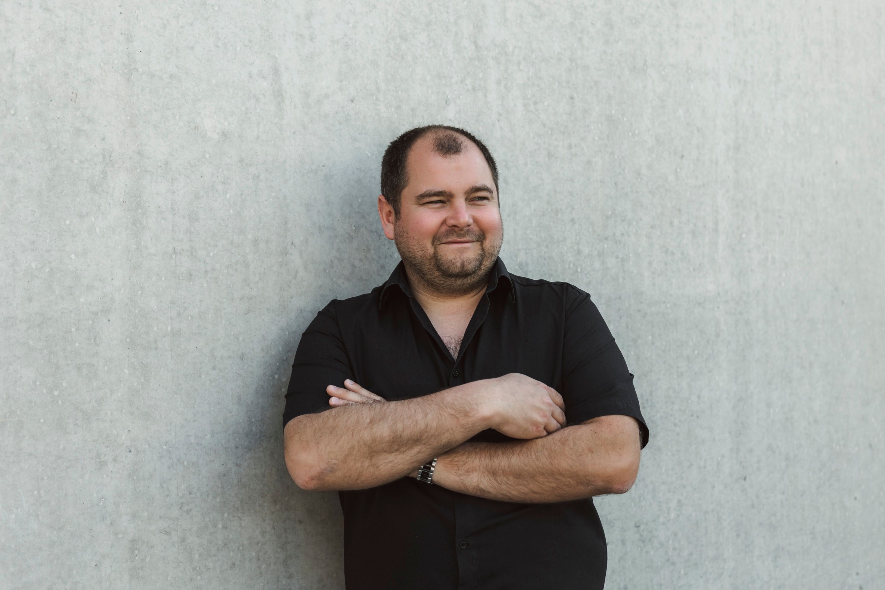 Man in a black shirt leaning against a concrete wall.