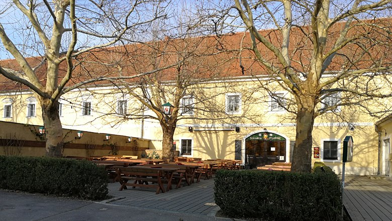 A yellow building with red roof tiles and a beer garden with wooden benches and tables in the foreground.