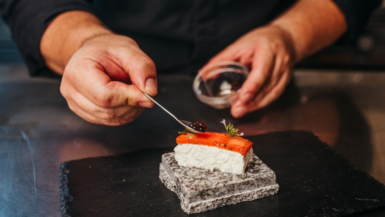 A chef decorates a piece of sushi with caviar on a stone.