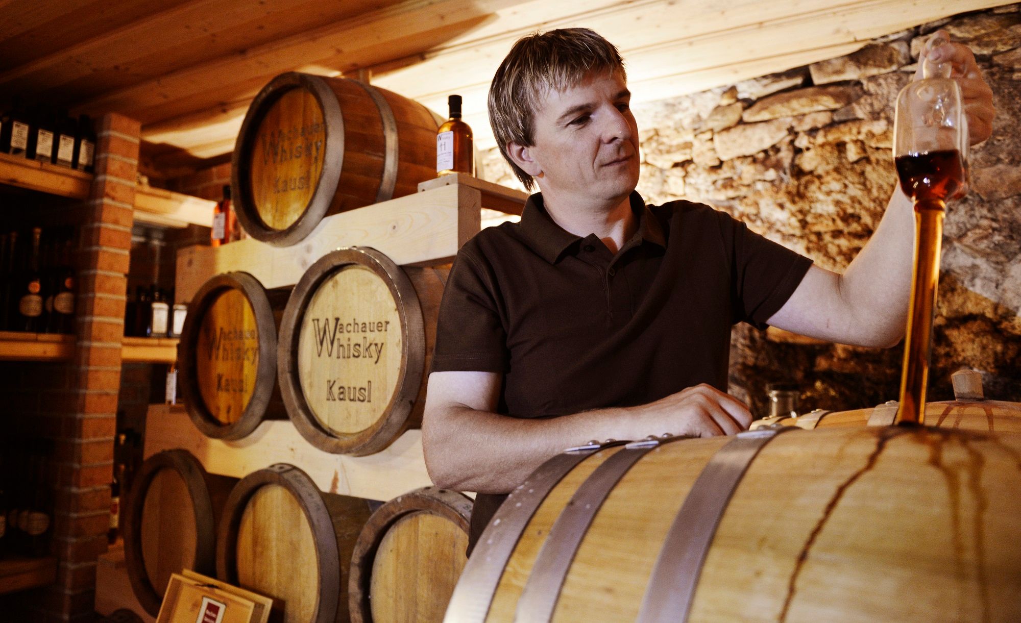 A man tasting whisky in a storage room with barrels.