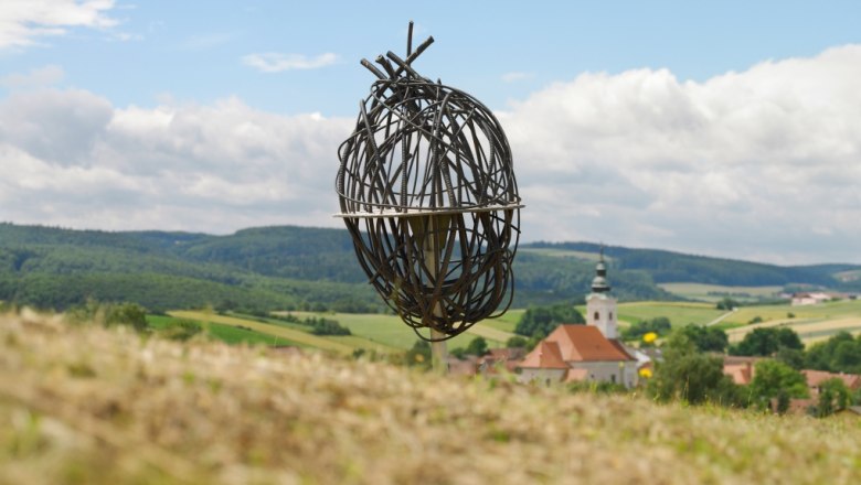 Metal art installation in a rural landscape with a church in the background.