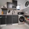 Modern kitchen with black cupboards, washing machine, microwave and coffee machine.