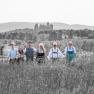 A group of six people in traditional dress stand in a field with a castle in the background.