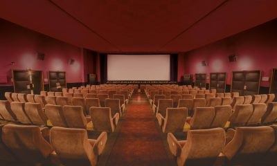 Empty movie theater with red walls and beige seats and screen