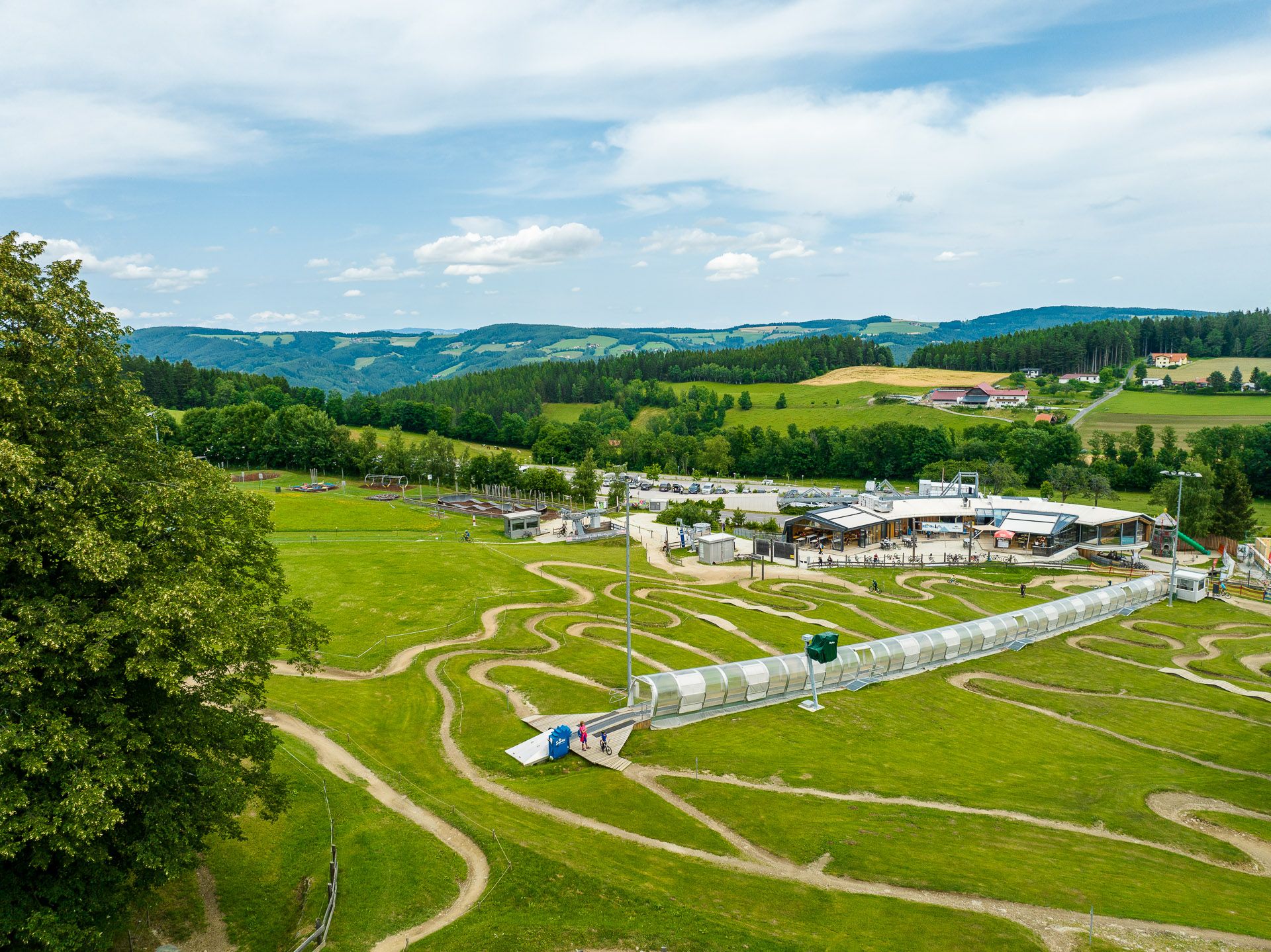 Aerial view of the Wexl Arena in St. Corona am Wechsel with green hills and a building in the background.