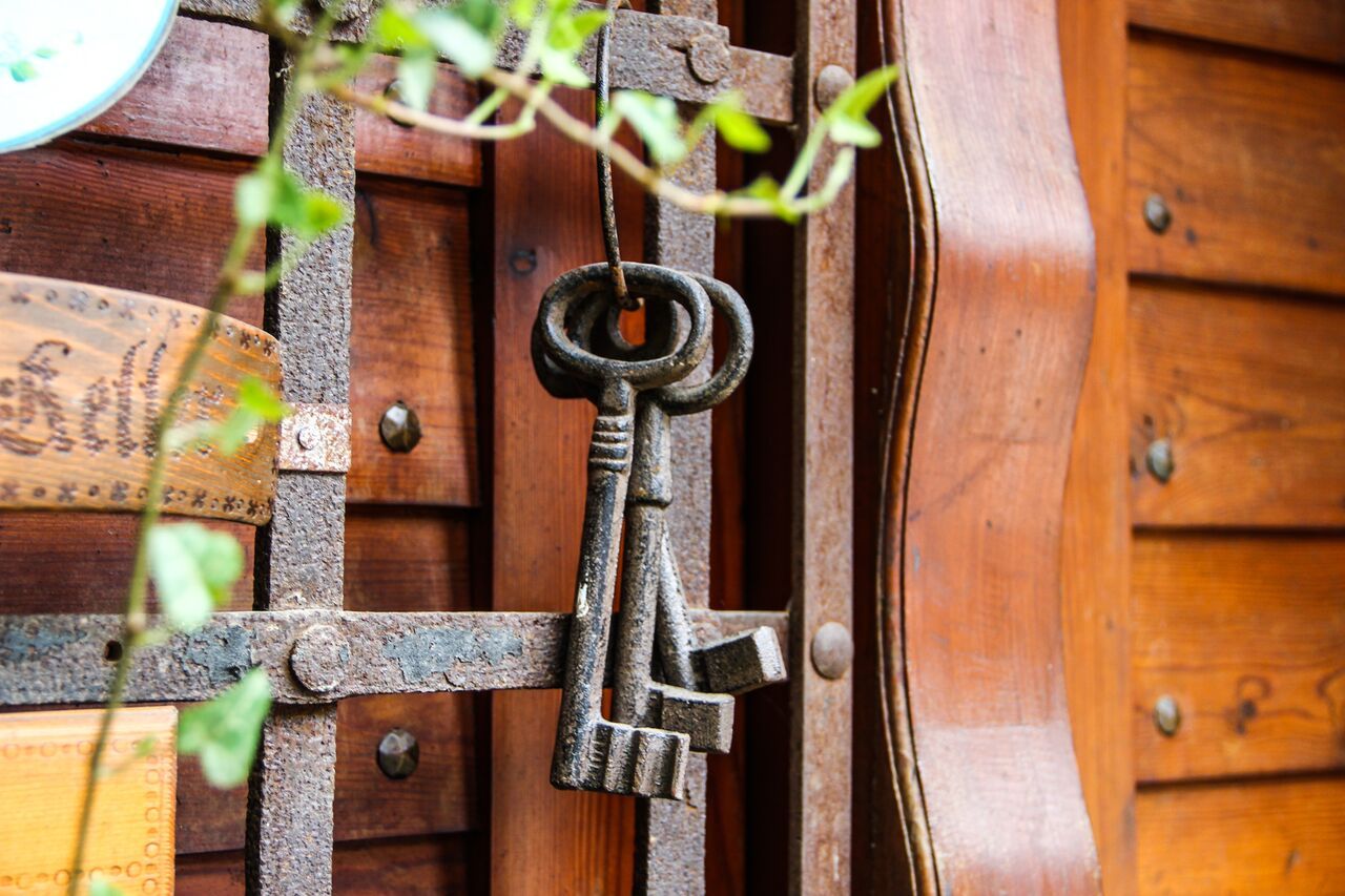 An old cellar key hangs on a rusty grille in front of a wooden wall.