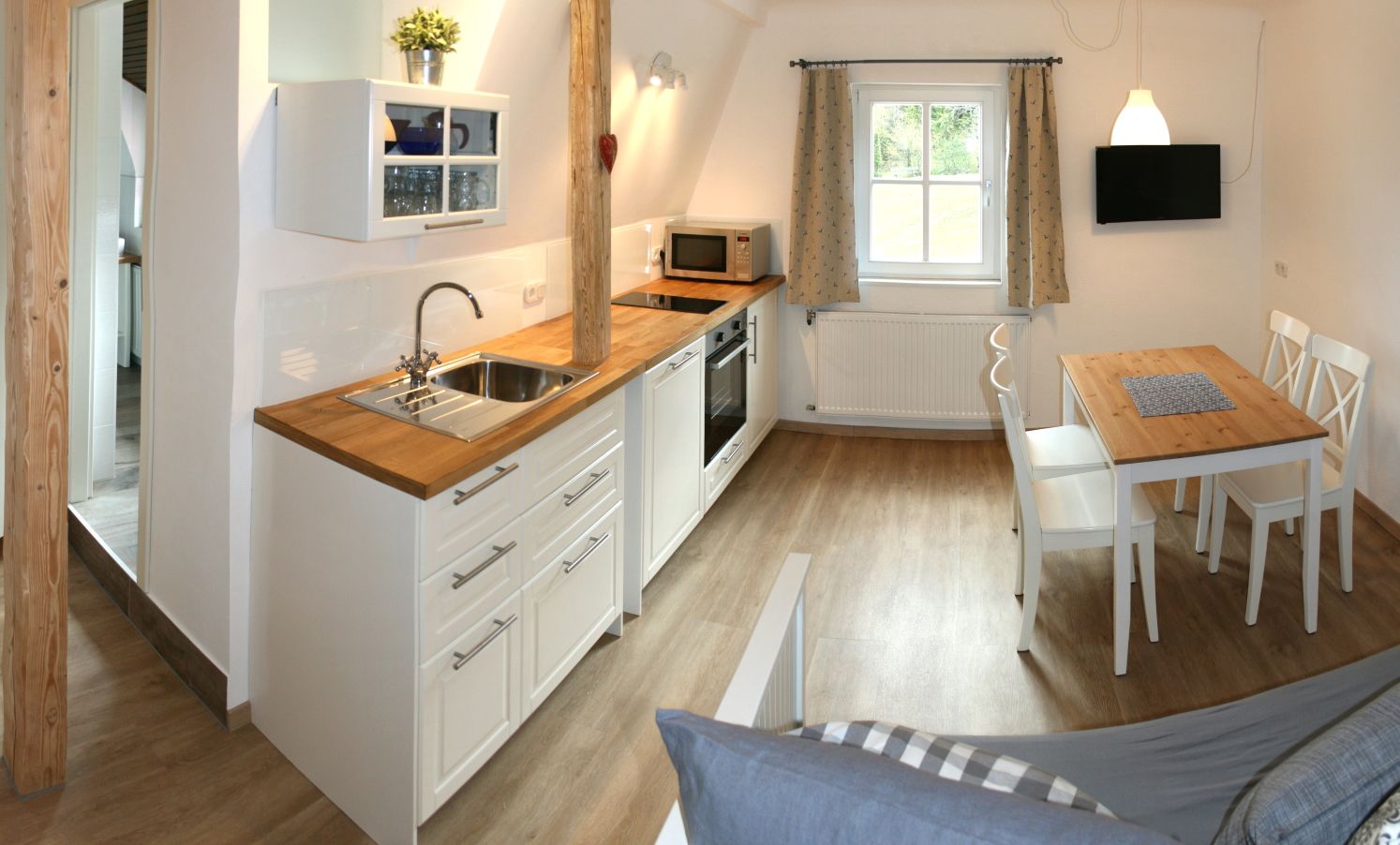 Modern kitchen with wooden floor, white cupboards, dining table and window.