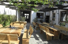 Wooden terrace with tables and benches under a pergola with vines.