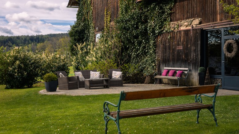 Garden area with seating furniture in front of a wooden building overgrown with ivy.