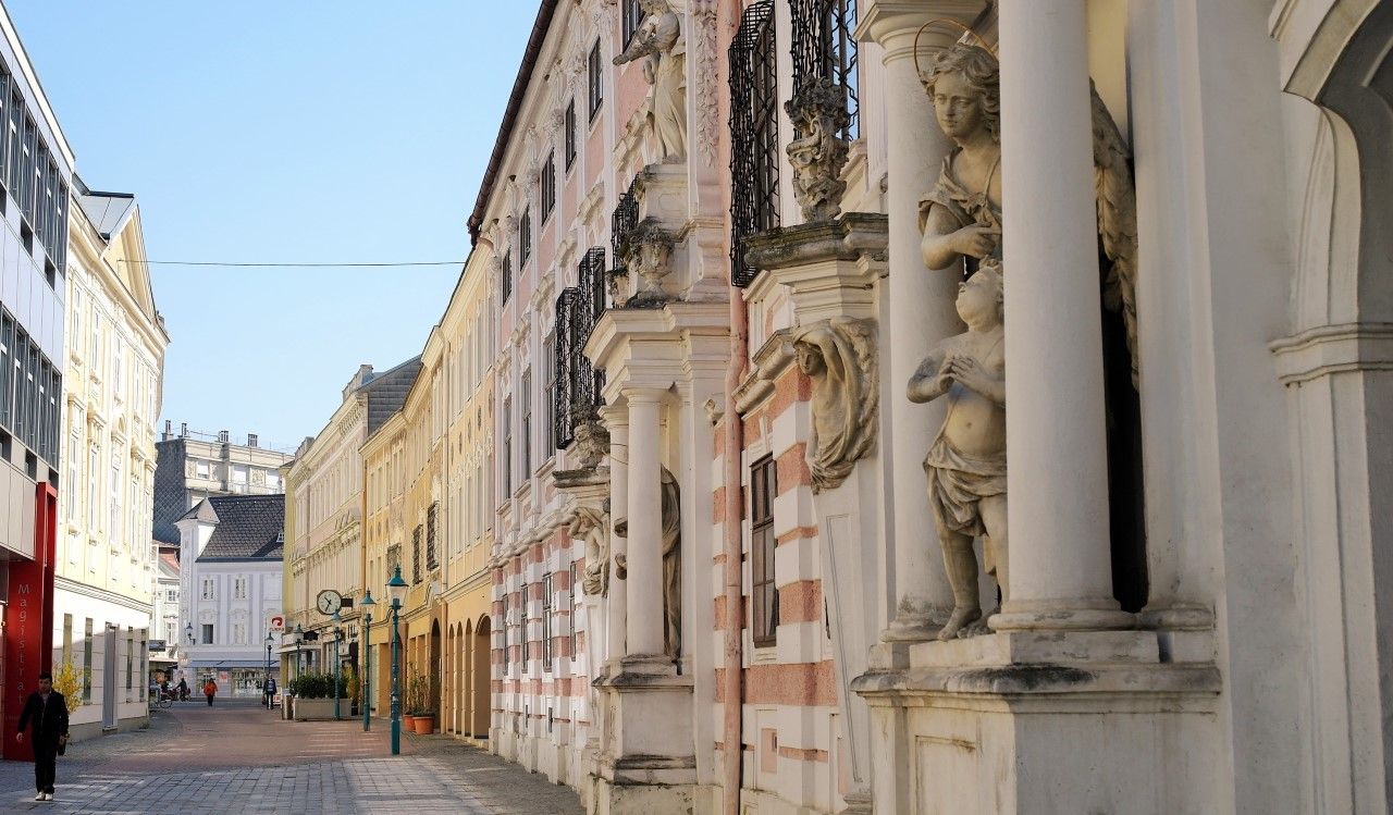 Street with historical buildings and statues in a city.