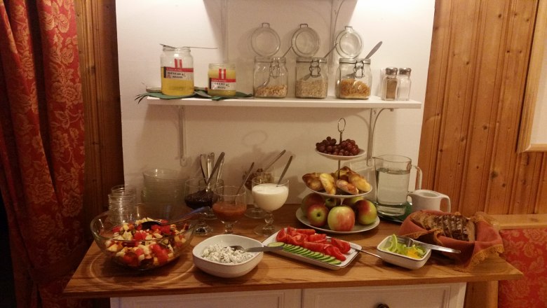 A breakfast buffet with fruit, bread, spreads and muesli in a cozy room.