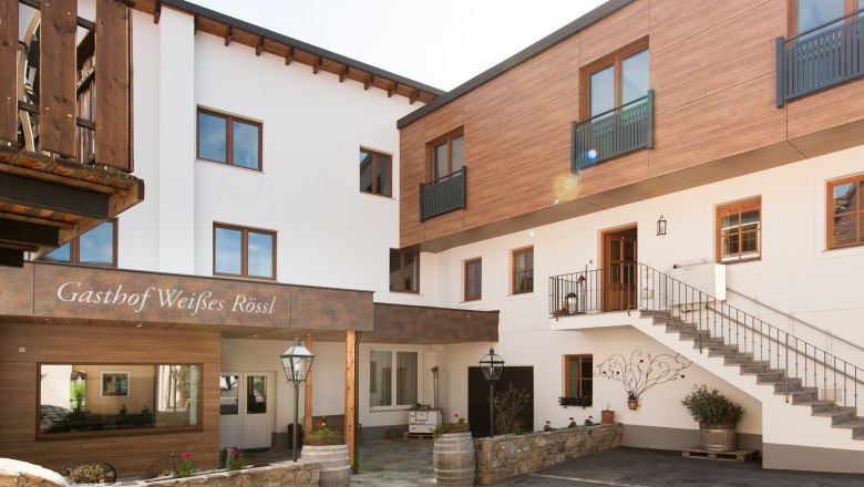 Exterior view of an inn with wooden and white facades, staircase and decorations.