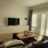 Modern living area with gray sofa, wooden table, carpet, TV and large windows with curtains.