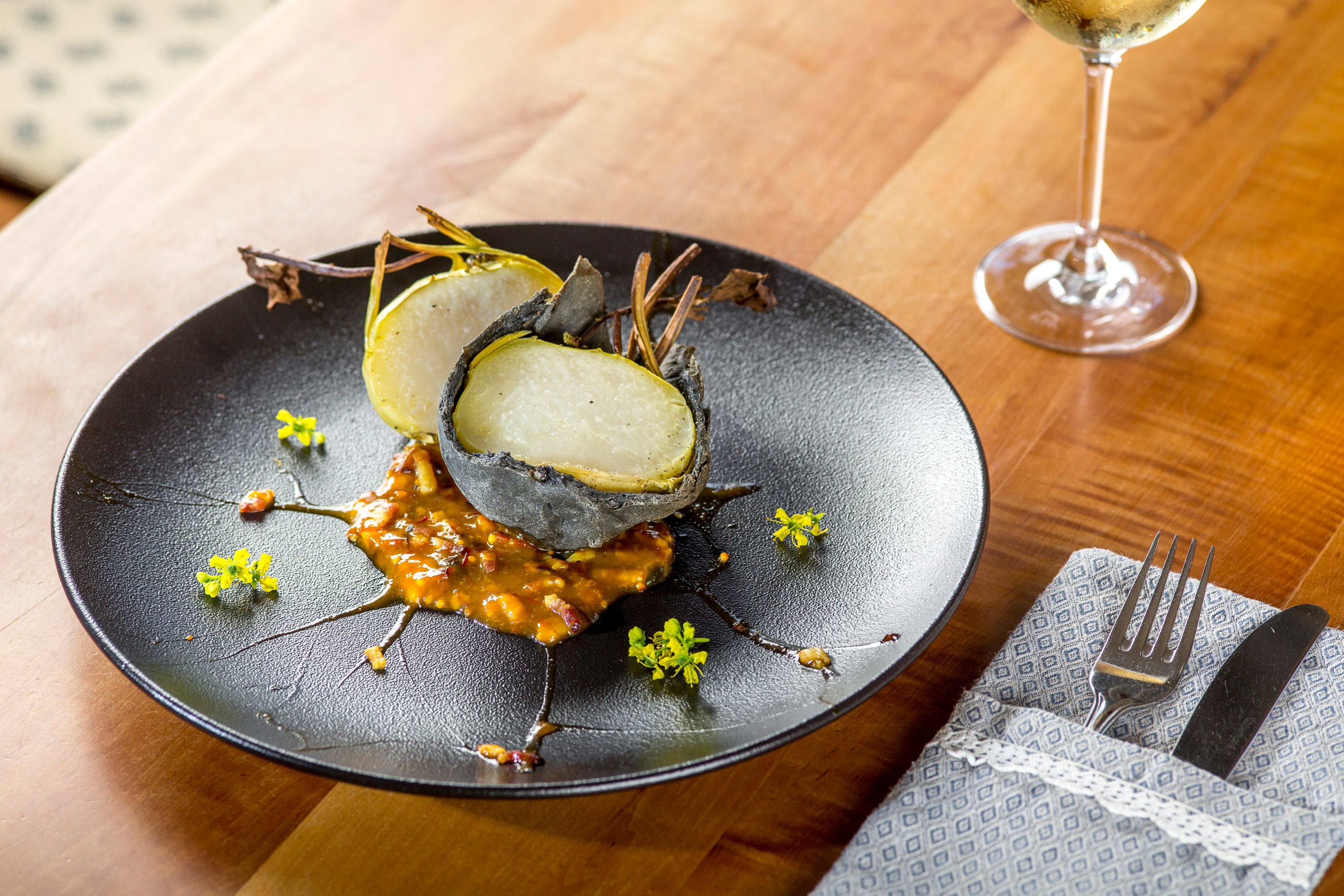 A dish of stone-crusted kohlrabi on bacon pear and Cider jam, served on a black plate with yellow flowers.