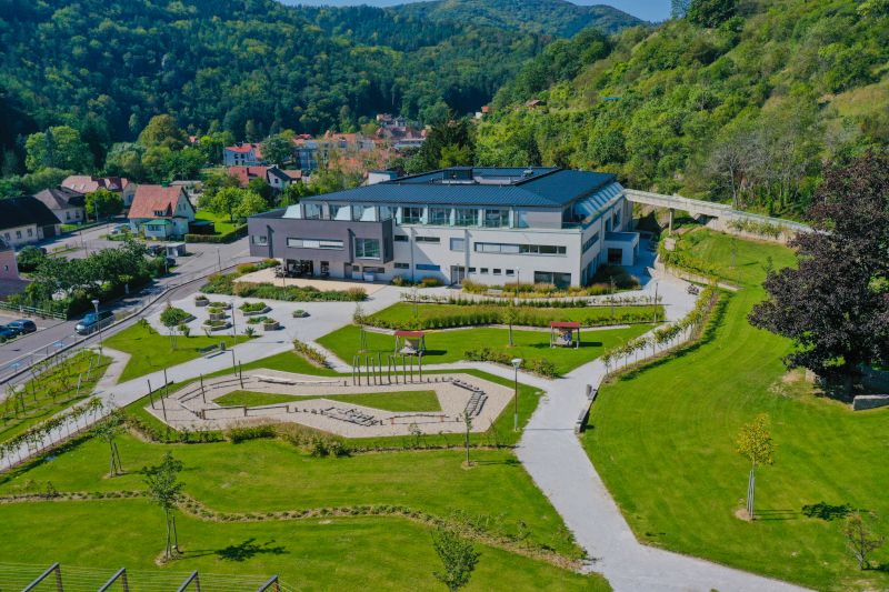 Aerial view of a modern building with garden, surrounded by green hills.