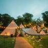 An illuminated teepee tent in a garden with fairy lights and trees at dusk.