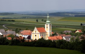 View of a church in Ottenthal with surrounding houses and wide fields in the background.