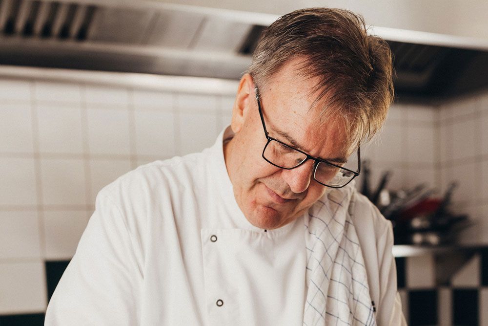 A chef in a white uniform works intently in a kitchen.