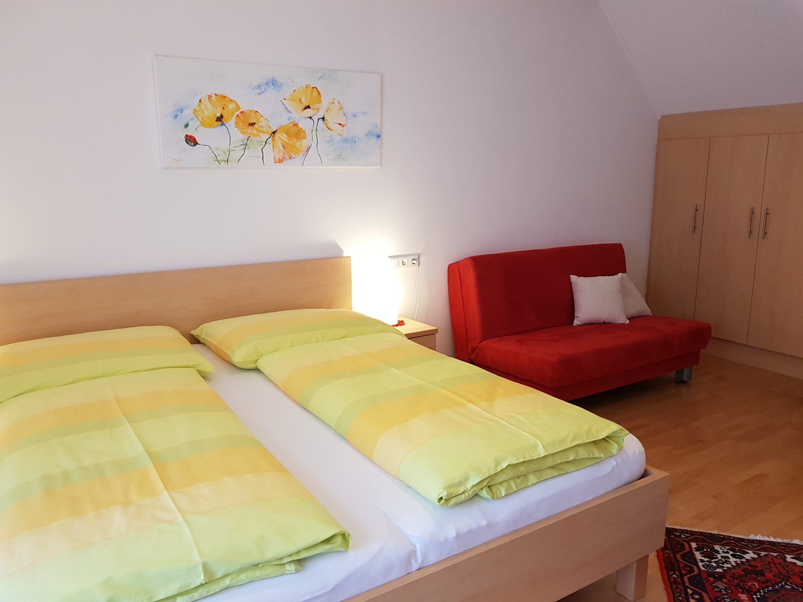 A double room with a bed, a red sofa, a wardrobe and a picture on the wall.