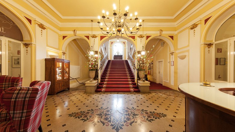 Elegant lobby with red carpet, staircase and chandelier.